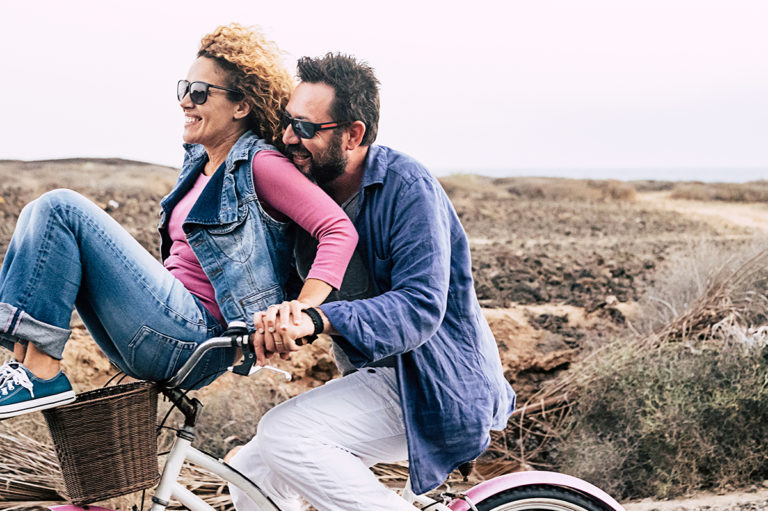 middle aged man driving a bicycle with woman sitting in the basket while they enjoy their successful financial management